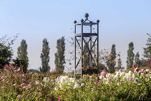 An Arthur Jack large steel obelisk pictured amongst plants in a garden